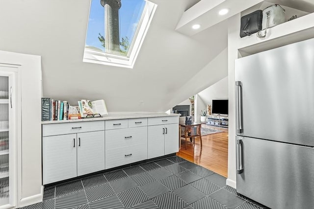 kitchen featuring stainless steel refrigerator, light countertops, white cabinetry, a skylight, and vaulted ceiling