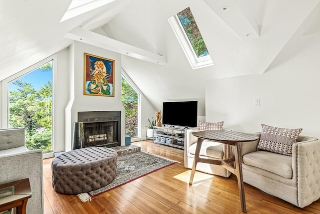 living room featuring a skylight, hardwood / wood-style floors, high vaulted ceiling, and a fireplace with raised hearth