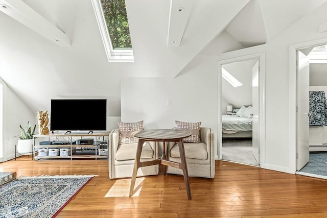 sitting room featuring a skylight, lofted ceiling, wood-type flooring, baseboard heating, and baseboards
