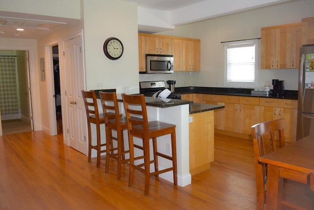 23 Beech St Unit 2, Framingham, MA 01702 - kitchen featuring appliances with stainless steel finishes, light brown cabinets, light wood-style flooring, a kitchen breakfast bar, and dark stone countertops