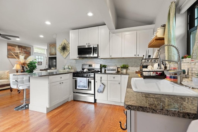 99 Lincoln St, Stoughton, MA 02072 - kitchen featuring appliances with stainless steel finishes, a peninsula, a sink, light wood-style flooring, and decorative backsplash