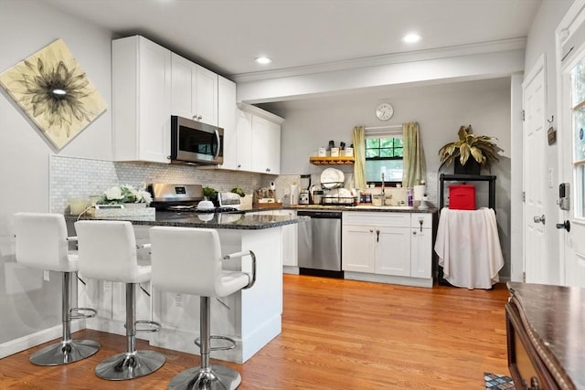 99 Lincoln St, Stoughton, MA 02072 - kitchen featuring stainless steel appliances, a peninsula, a breakfast bar area, tasteful backsplash, and white cabinets