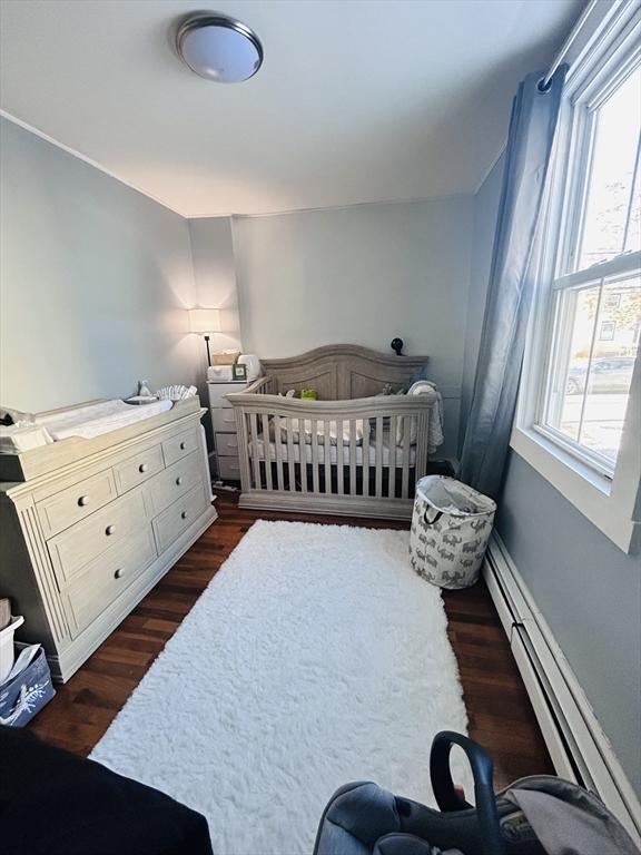 bedroom featuring dark hardwood / wood-style flooring, a crib, and baseboard heating