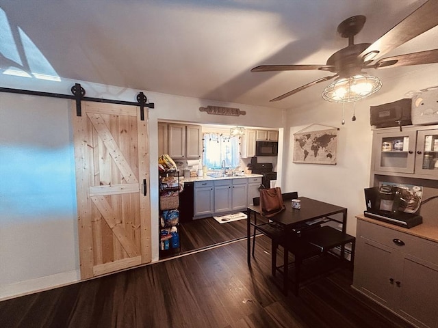 kitchen featuring dark wood-type flooring, sink, black range oven, ceiling fan, and a barn door