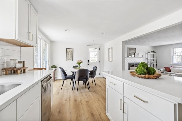 kitchen with light countertops, backsplash, stainless steel dishwasher, open floor plan, and white cabinetry