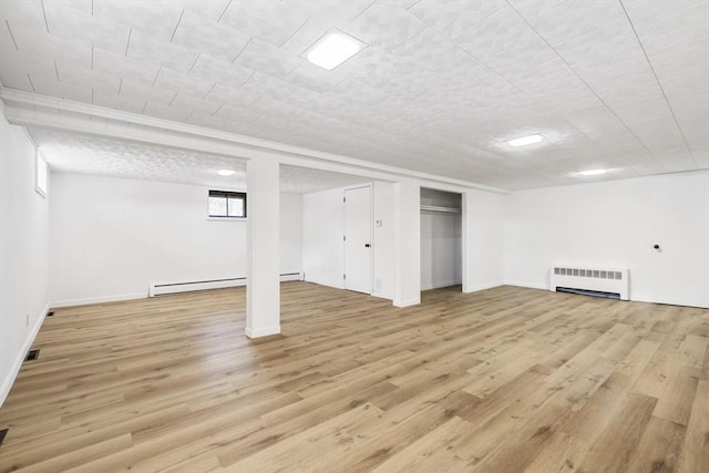 below grade area with baseboards, visible vents, radiator, baseboard heating, and light wood-style floors