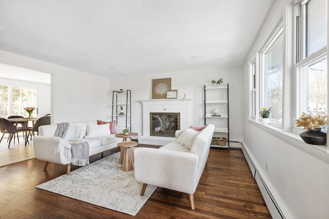 living area with dark wood-type flooring, baseboard heating, a fireplace, and baseboards