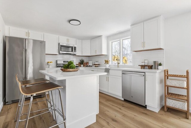 kitchen with a kitchen island, white cabinetry, stainless steel appliances, and light countertops