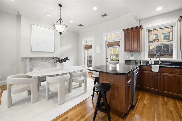 kitchen featuring stainless steel dishwasher, a breakfast bar, crown molding, wood-type flooring, and hanging light fixtures