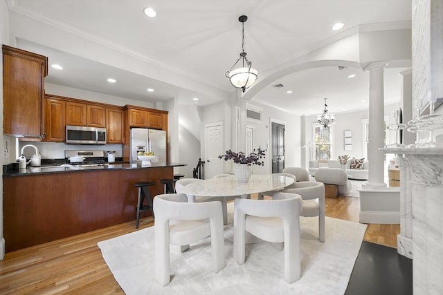 dining space featuring sink, crown molding, a notable chandelier, light hardwood / wood-style floors, and decorative columns