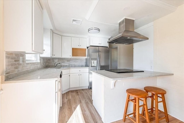 kitchen featuring white cabinetry, a breakfast bar area, stainless steel fridge, island exhaust hood, and black electric cooktop