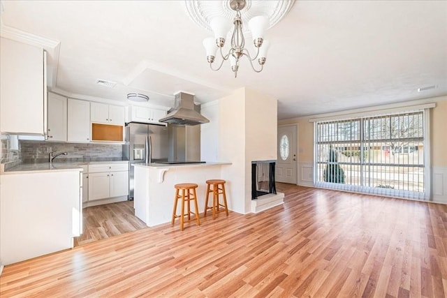 kitchen featuring a multi sided fireplace, pendant lighting, white cabinets, island exhaust hood, and light hardwood / wood-style floors