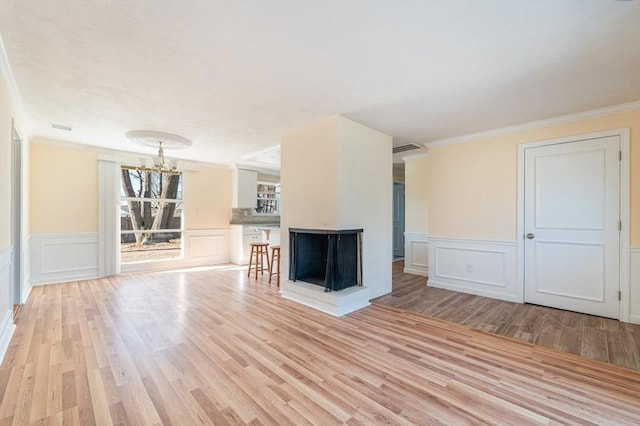 unfurnished living room with a notable chandelier, ornamental molding, light hardwood / wood-style floors, and a multi sided fireplace