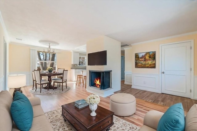 living room with hardwood / wood-style flooring, crown molding, a multi sided fireplace, and an inviting chandelier