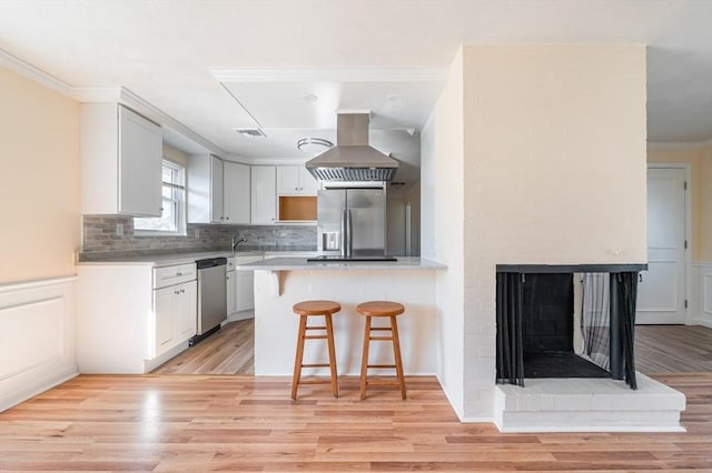 kitchen featuring white cabinetry, a kitchen breakfast bar, island exhaust hood, kitchen peninsula, and stainless steel appliances