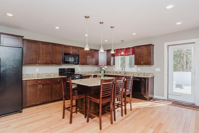 kitchen featuring a breakfast bar area, black appliances, decorative light fixtures, light hardwood / wood-style floors, and a center island