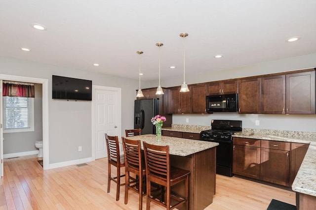 kitchen featuring a breakfast bar area, light stone counters, black appliances, decorative light fixtures, and a center island