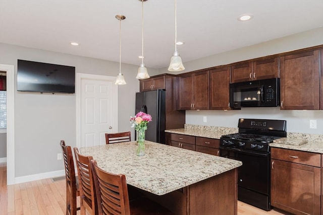 kitchen with a breakfast bar area, a kitchen island, pendant lighting, and black appliances