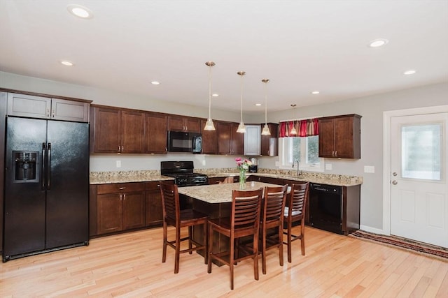 kitchen featuring decorative light fixtures, a kitchen bar, black appliances, and light hardwood / wood-style flooring