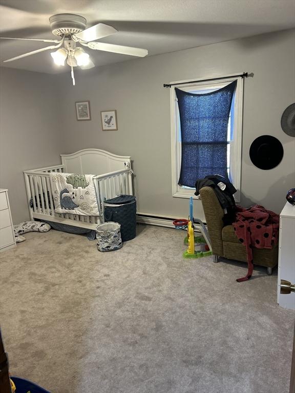 carpeted bedroom with ceiling fan, a nursery area, and a baseboard radiator