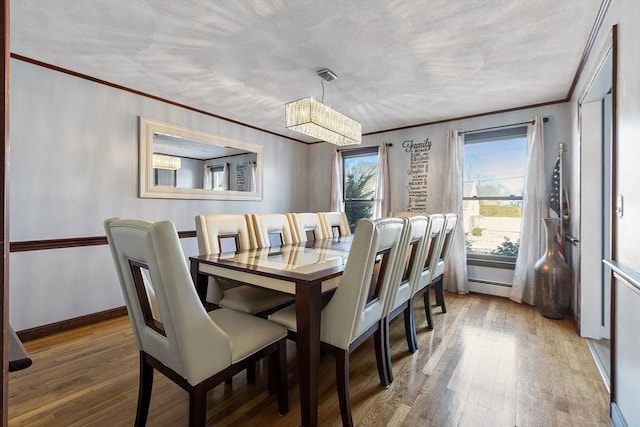 dining room featuring baseboard heating, a textured ceiling, wood-type flooring, an inviting chandelier, and ornamental molding