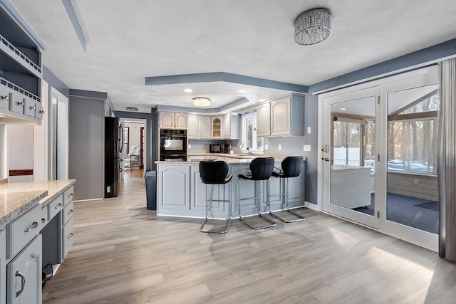 kitchen with a kitchen bar, light wood-type flooring, light stone countertops, double oven, and sink