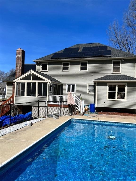 back of house with a sunroom, a swimming pool side deck, and solar panels