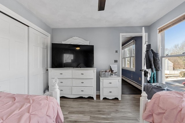 bedroom featuring dark wood-type flooring, ceiling fan, a closet, and baseboard heating