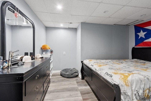 bedroom with a drop ceiling and light wood-type flooring