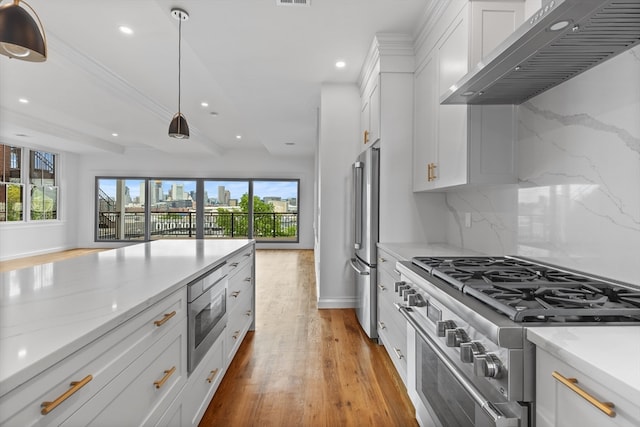 kitchen with light hardwood / wood-style floors, stainless steel appliances, hanging light fixtures, tasteful backsplash, and wall chimney exhaust hood