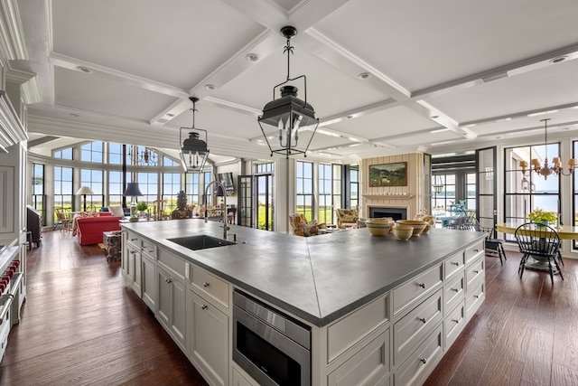 kitchen featuring stainless steel microwave, a wealth of natural light, a center island with sink, and sink