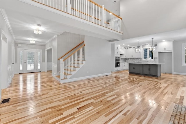 unfurnished living room featuring crown molding, a towering ceiling, light hardwood / wood-style flooring, and a chandelier