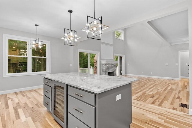 kitchen with gray cabinets, a fireplace, decorative light fixtures, beverage cooler, and a center island