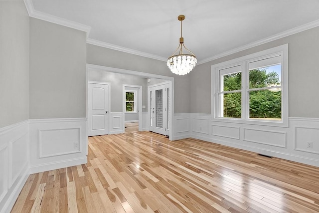 unfurnished dining area with ornamental molding, a wealth of natural light, an inviting chandelier, and light hardwood / wood-style flooring