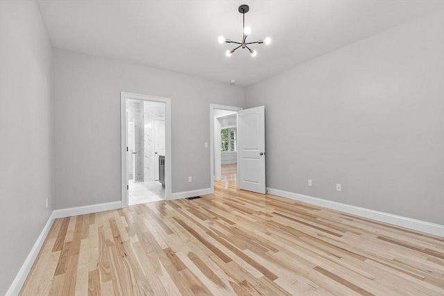 spare room featuring a chandelier and light hardwood / wood-style flooring