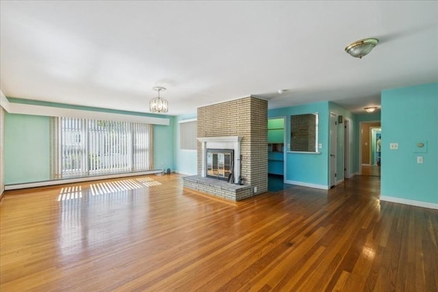 7 Wilbur Ct, Saugus, MA 01906 - unfurnished living room featuring a baseboard heating unit, a chandelier, wood finished floors, a brick fireplace, and baseboards