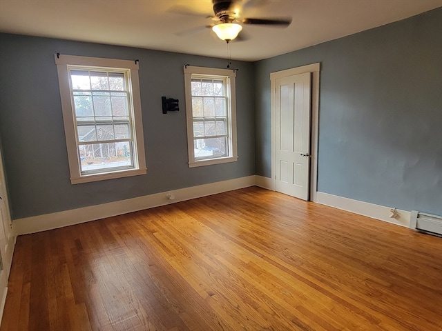 empty room with ceiling fan, a healthy amount of sunlight, light wood-type flooring, and a baseboard heating unit