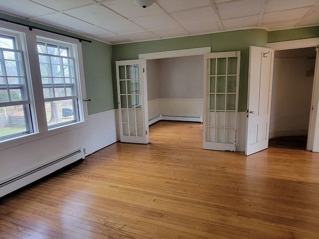 unfurnished room featuring baseboard heating, light hardwood / wood-style flooring, and a drop ceiling