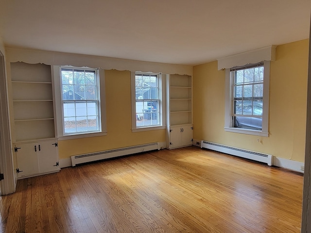 empty room featuring light wood-type flooring, baseboard heating, and a healthy amount of sunlight