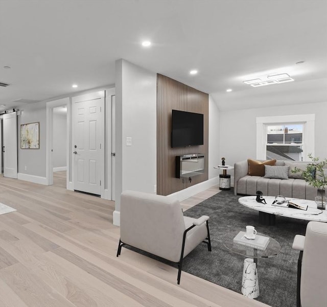 living room featuring recessed lighting, baseboards, a barn door, and light wood-style flooring
