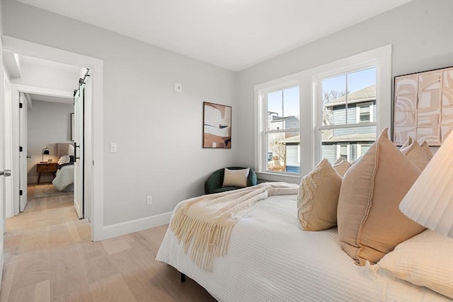 bedroom with baseboards, a barn door, and light wood-style floors