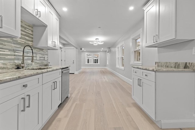 kitchen with stainless steel dishwasher, baseboards, white cabinets, a sink, and backsplash