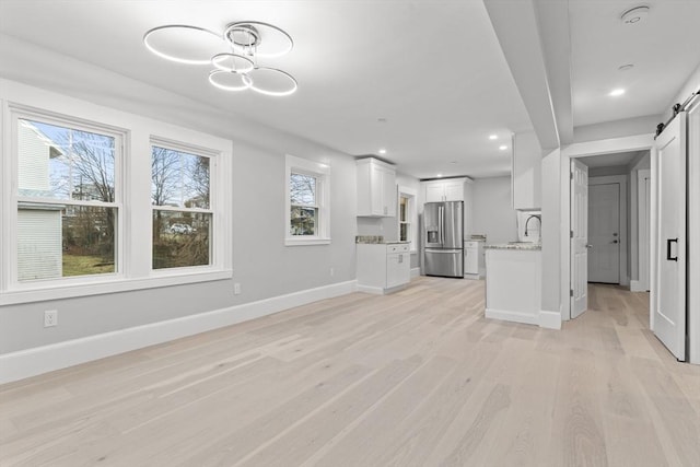 unfurnished living room featuring a sink, baseboards, light wood-style flooring, and a barn door