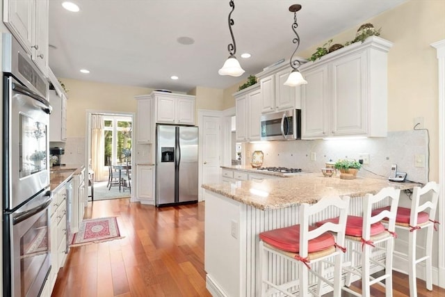 kitchen featuring stainless steel appliances, a peninsula, light wood finished floors, light stone countertops, and tasteful backsplash
