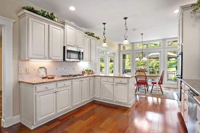 kitchen with stainless steel appliances, dark wood finished floors, white cabinets, backsplash, and a peninsula