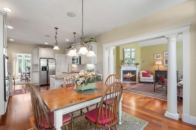 dining area with wood finished floors, decorative columns, a lit fireplace, and recessed lighting