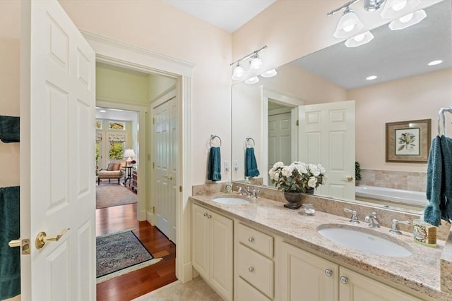 ensuite bathroom with double vanity, a garden tub, and wood finished floors