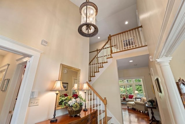 stairs featuring a high ceiling, decorative columns, baseboards, and wood finished floors