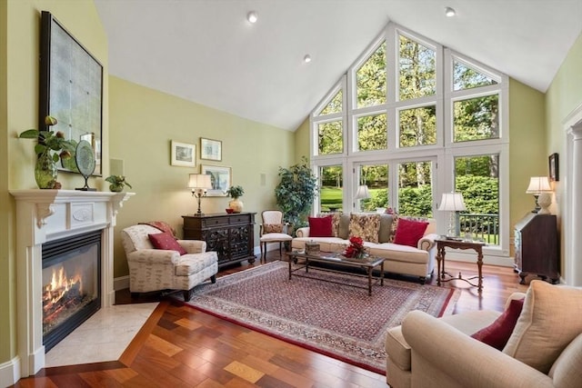 living room featuring a fireplace with flush hearth, high vaulted ceiling, wood finished floors, and baseboards