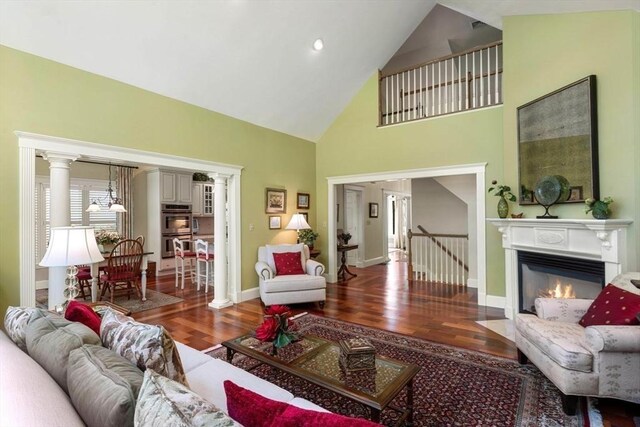 living room featuring wood finished floors, high vaulted ceiling, baseboards, and a fireplace with flush hearth